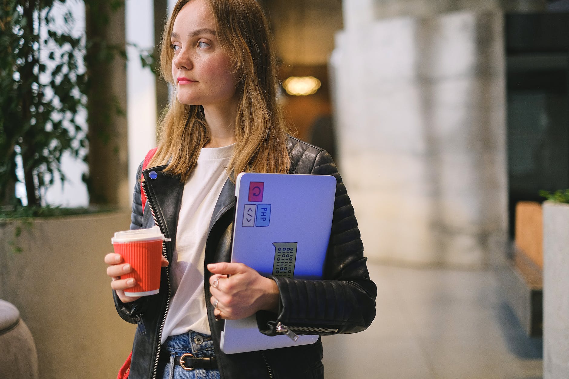 photo of a young woman holding a coffee cup and a laptop and looking away