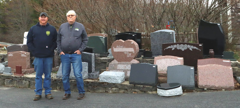 Casey Stevens (left) and his father, Thomas Stevens, founder of Thomas A. Stevens Cemetery Memorials and Cemetery Restoration, stand in front of display pieces at the business, now known as Stevens Monuments & Granite Works, at 10 Lynch Road in Newcastle. (Piper Pavelich photo)