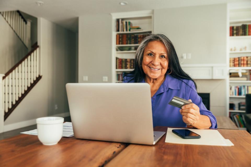 A woman holding a credit card and looking at her computer.